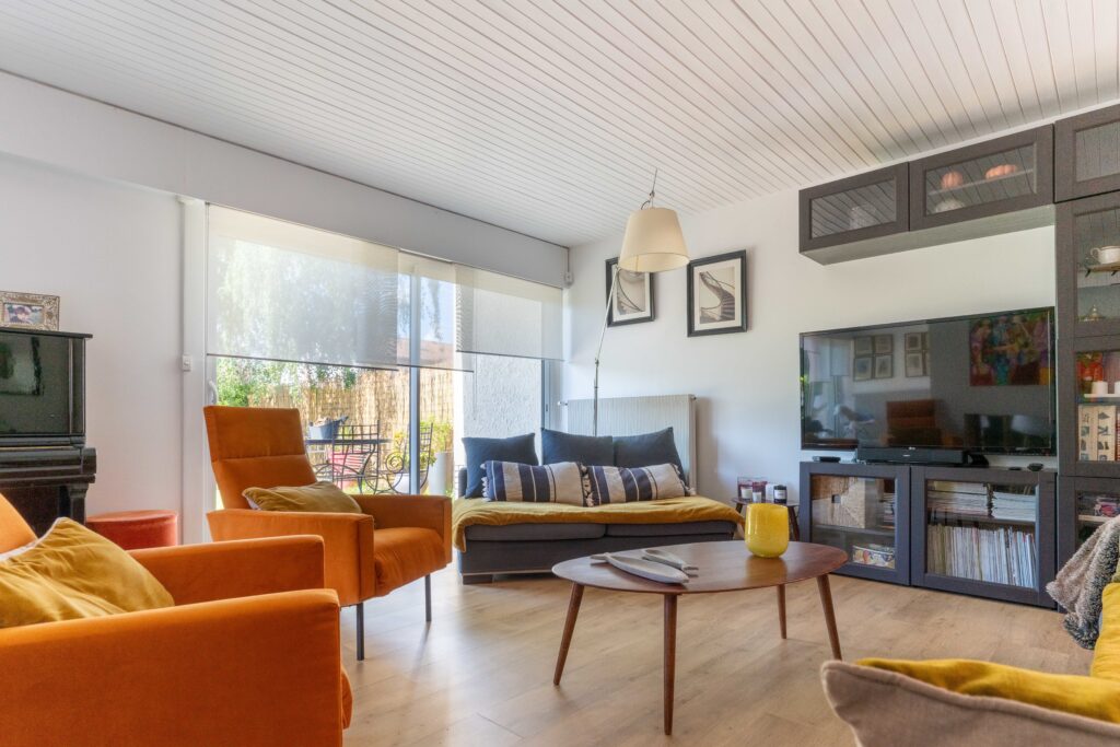 Un salon dans lequel il y a du mobilier de couleurs et une baie vitré qui donne sur l'extérieur