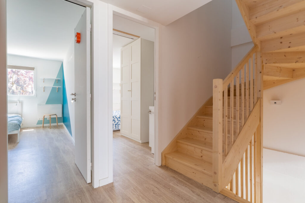 Il y a un palier d'étage qui s'ouvre sur deux chambres avec un escalier en bois.