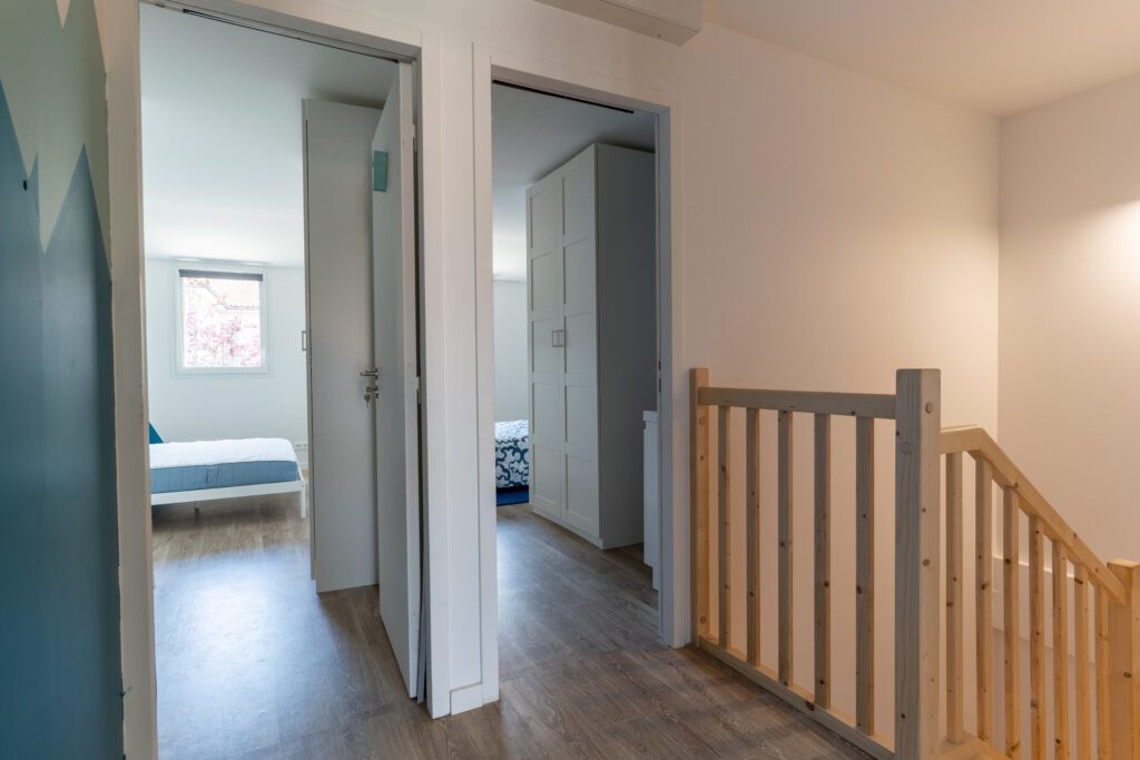 Un palier de chambre qui donne sur deux chambres qui ont les portes ouvertes. Il y a une rambarde en bois. un sol en bois