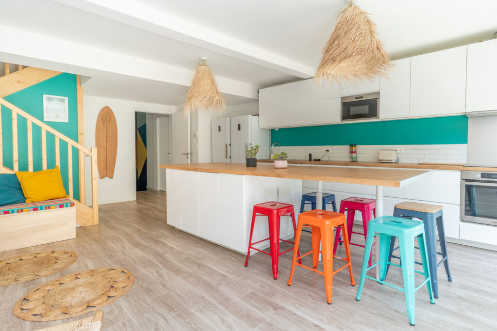 Une grande cuisine lumineuse, avec des tabourets de plusieurs couleurs différentes.