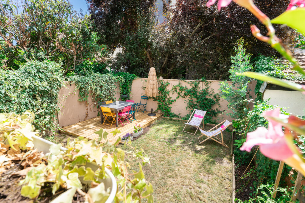 Une cour extérieure clos sans vis avis. il ya une terrasse bois, avec une table et des chaises avec des transats à l'abri du soleil.