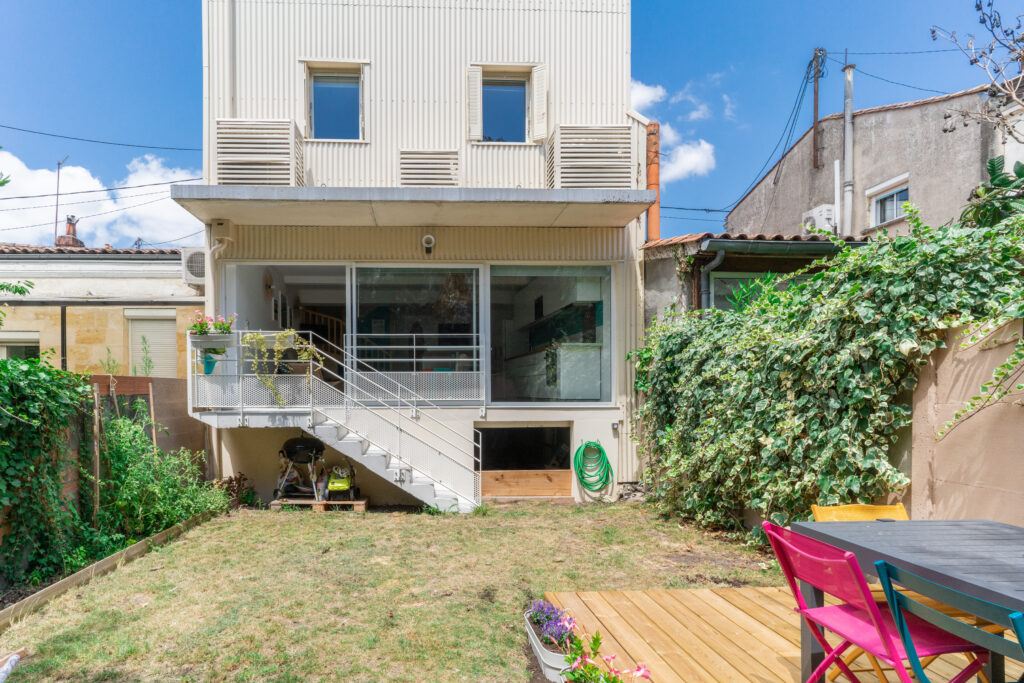 Façade d'une maison à étage avec un petit jardin en premier plan et un escalier en façade.