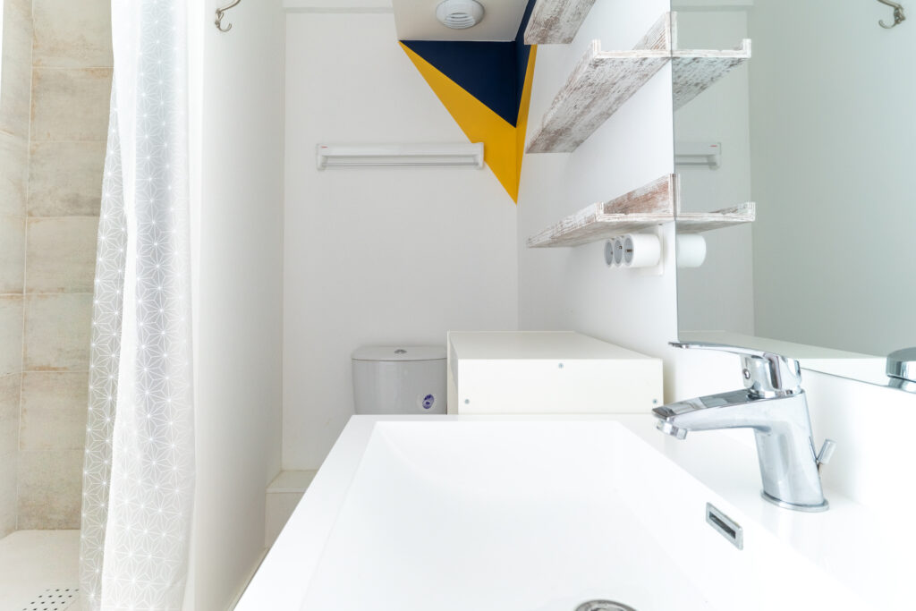 Une petite salle de bain blanche, bleue et jaune avec l'évier en premier plan