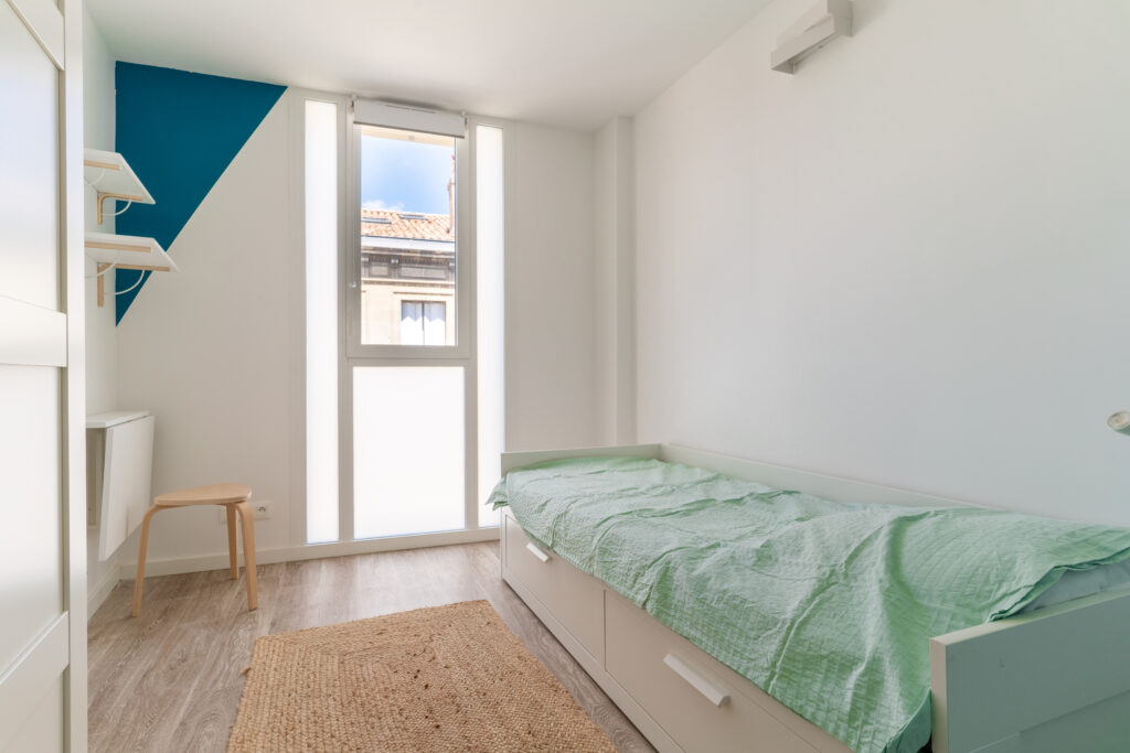Une chambre avec un lit simple et une couverture verte